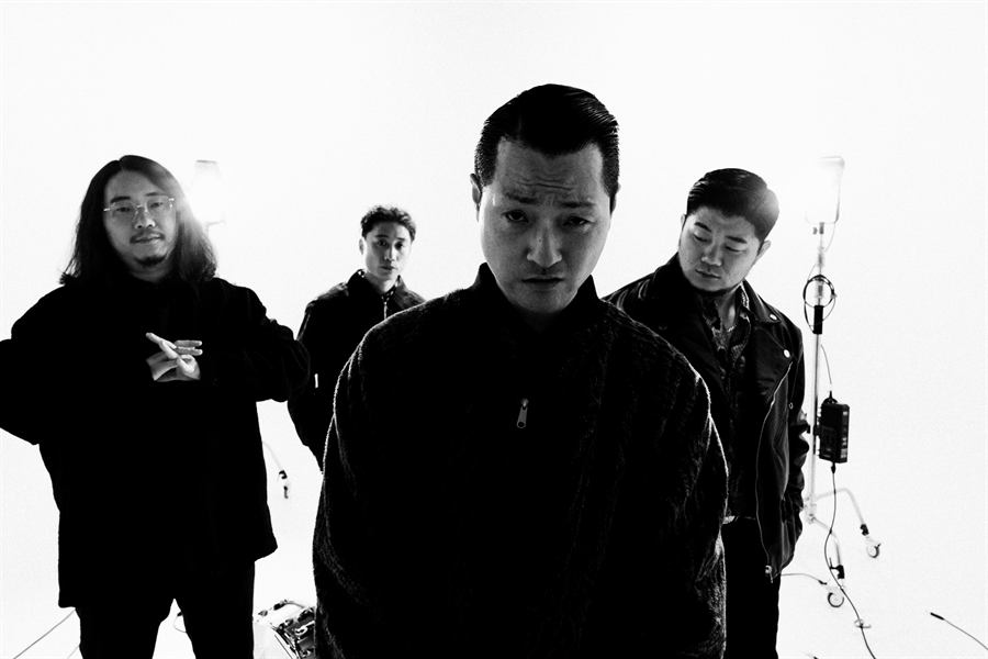 흰 배경 앞에 검은 옷을 입고 선 네 멤버